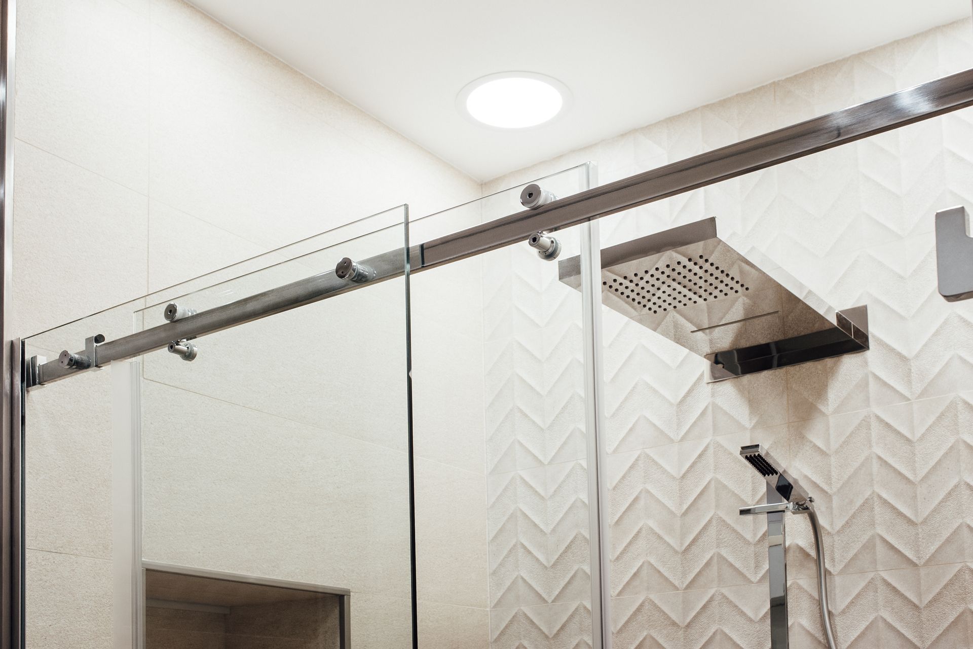 Close-up of a modern shower with glass doors and a square rainfall showerhead.