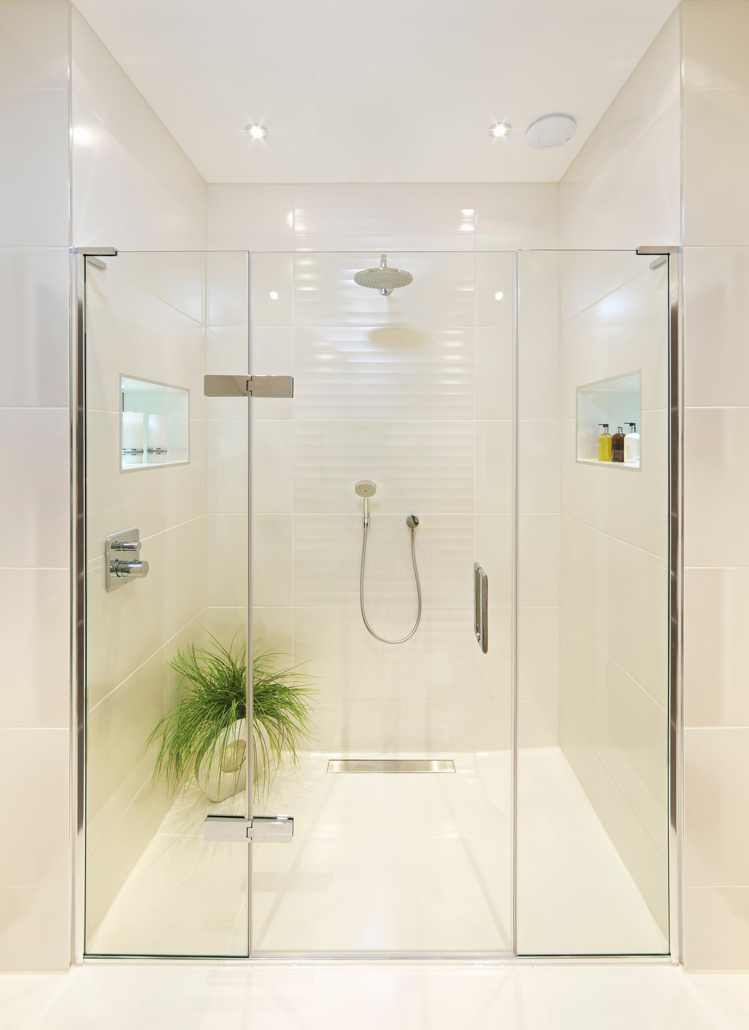 White tiled bathroom with a wide transparent shower door and a green plant in one of the sides. White tiled bathroom with a wide transparent shower door and a green plant in one of the sides.