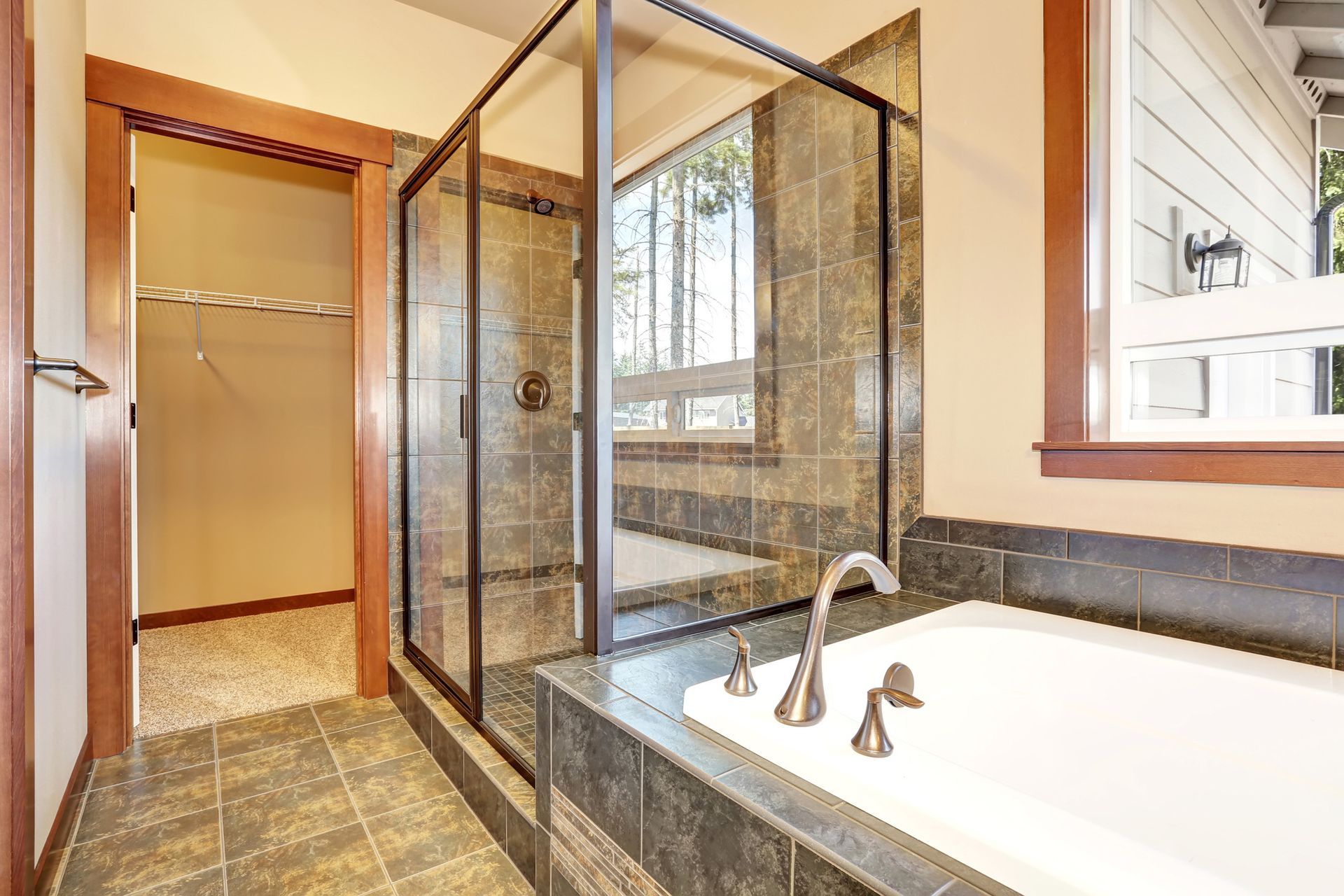 Modern bathroom with tiled shower enclosure and soaking tub near bright window in clean interior spa.