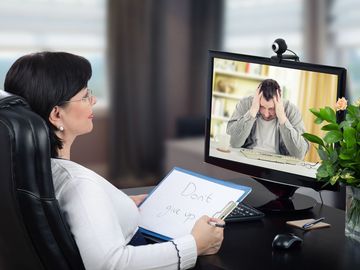 A woman is sitting in front of a computer talking to a man.