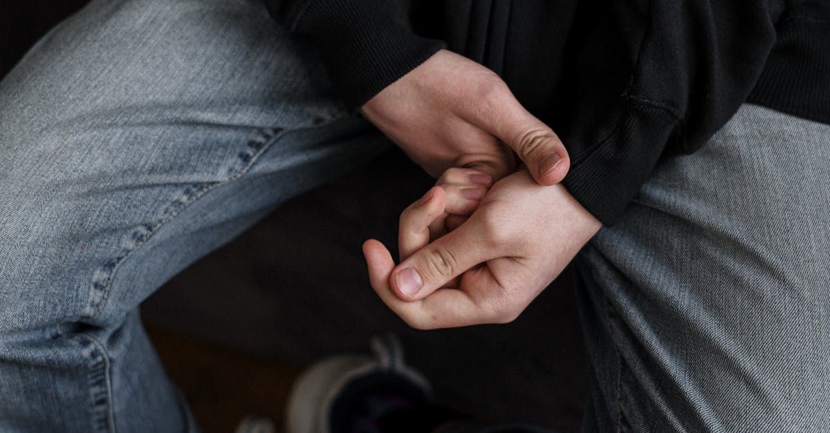 A person is sitting down and holding their hands together.