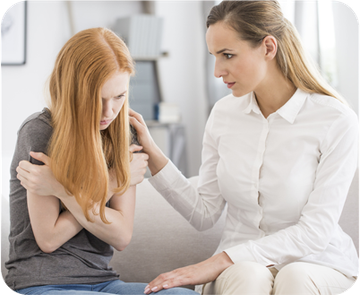 A woman is comforting another woman who is sitting on a couch.