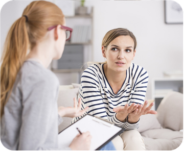 A woman is sitting on a couch talking to another woman.