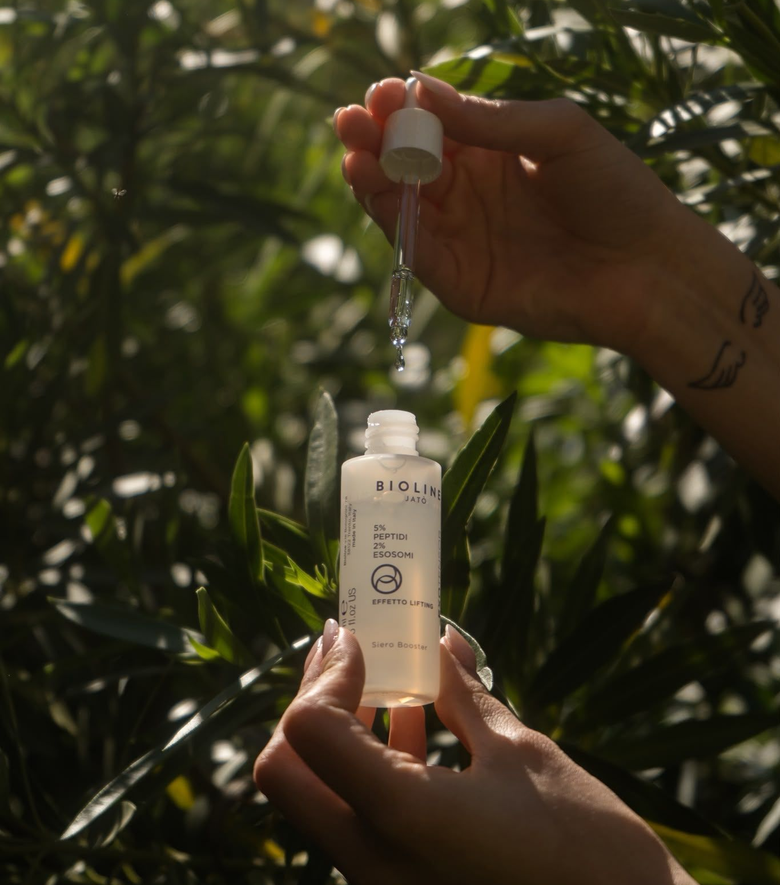 Mani che erogano siero in una piccola boccetta per prodotti per la cura della pelle tra la vegetazione verde all'aperto