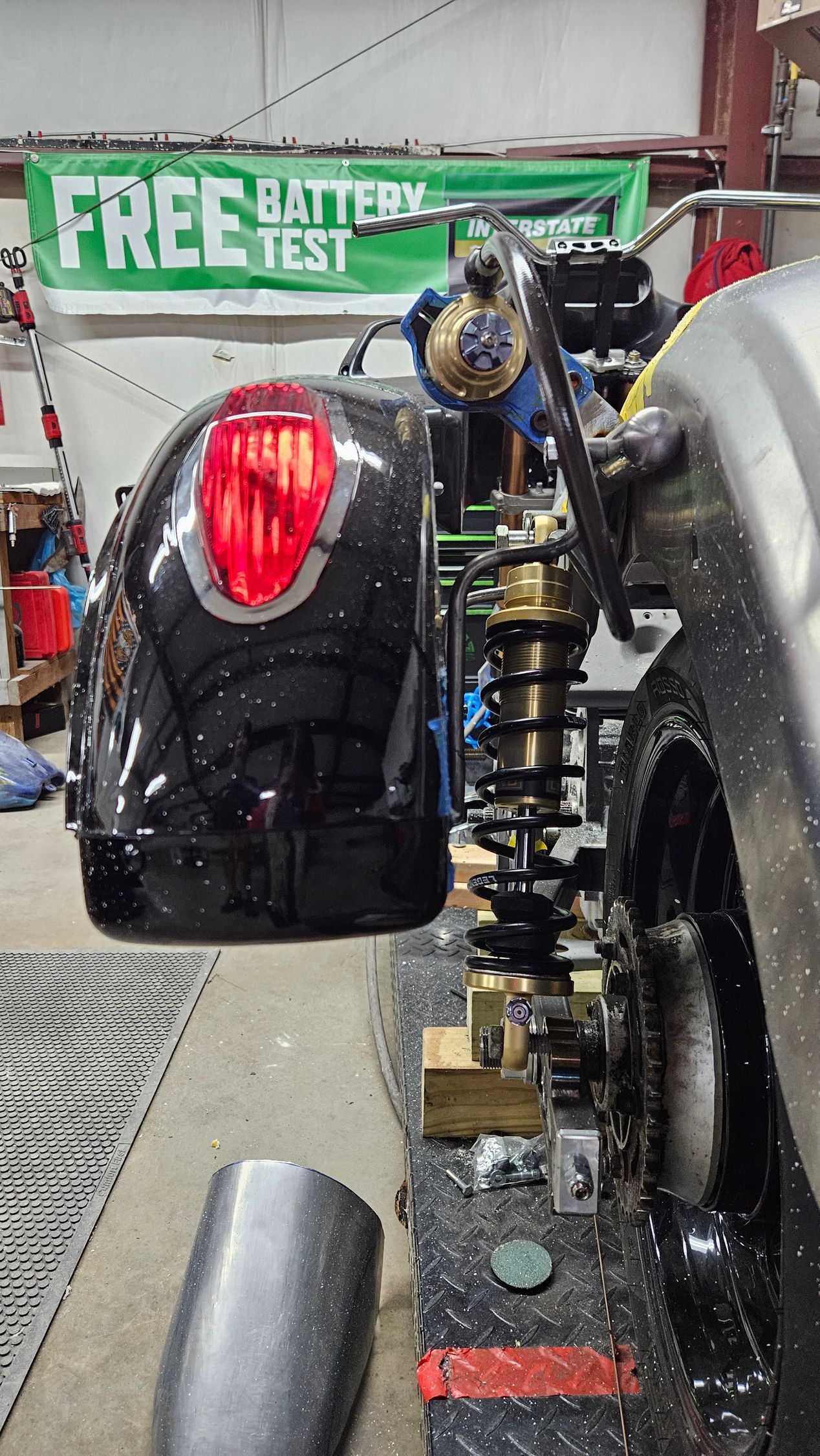 A motorcycle is sitting in a garage next to a free battery test sign.