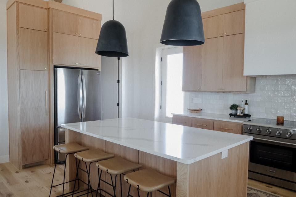 A kitchen with a large island , stools , a refrigerator and a stove.