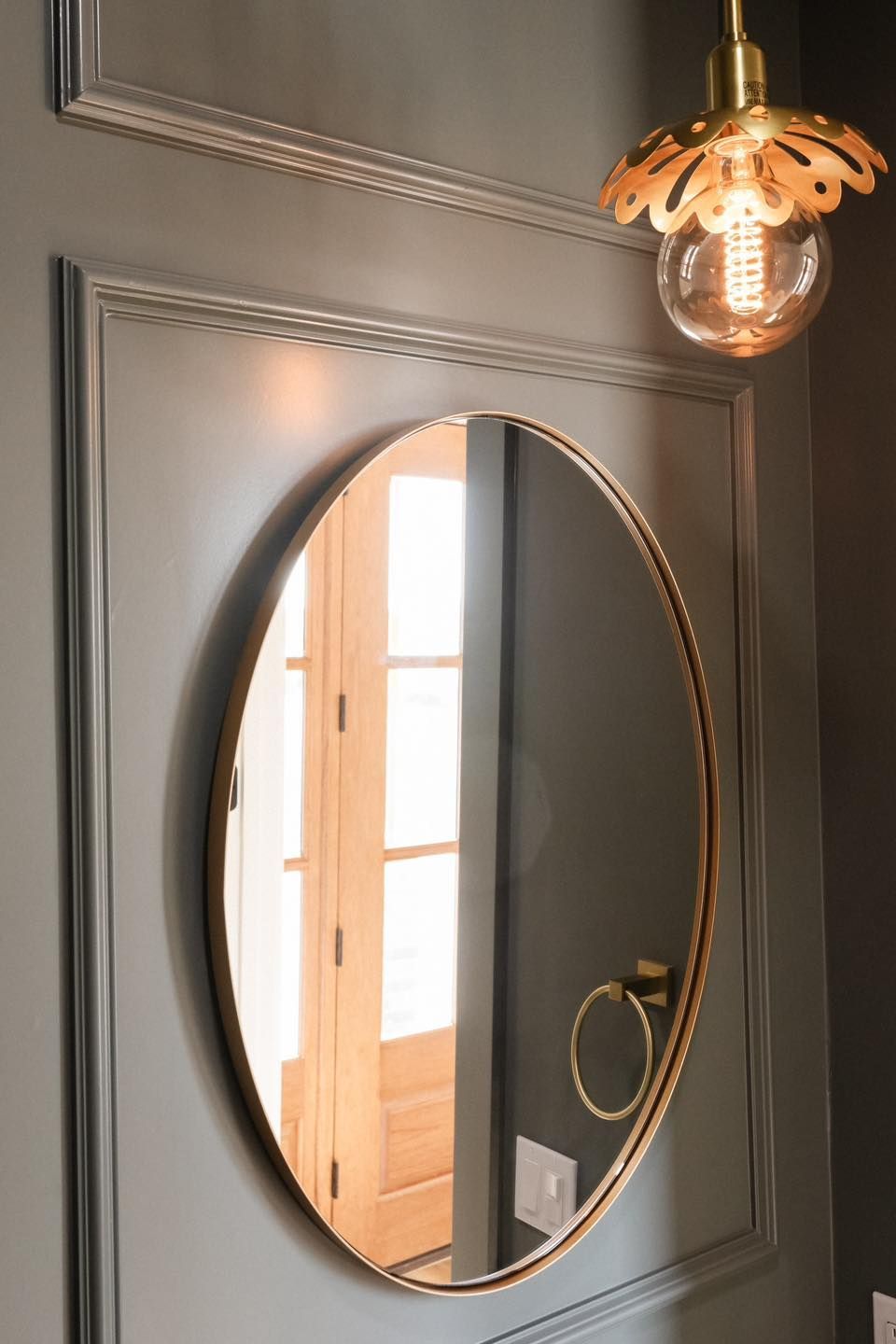 A round mirror is hanging on a wall next to a light bulb.