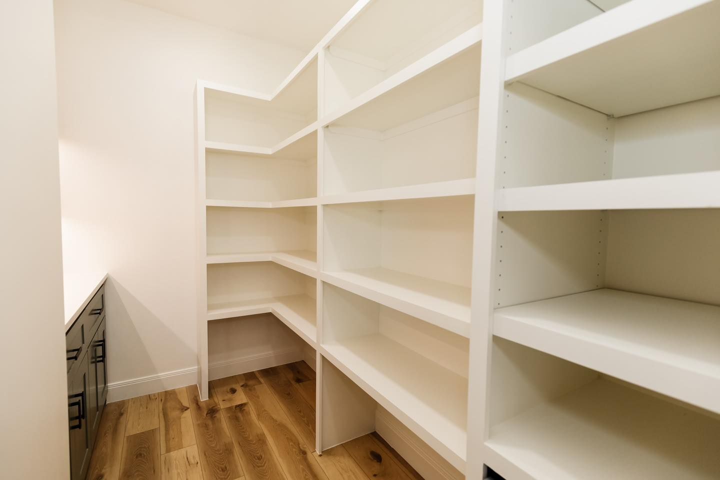 A walk in pantry with lots of shelves and wooden floors.
