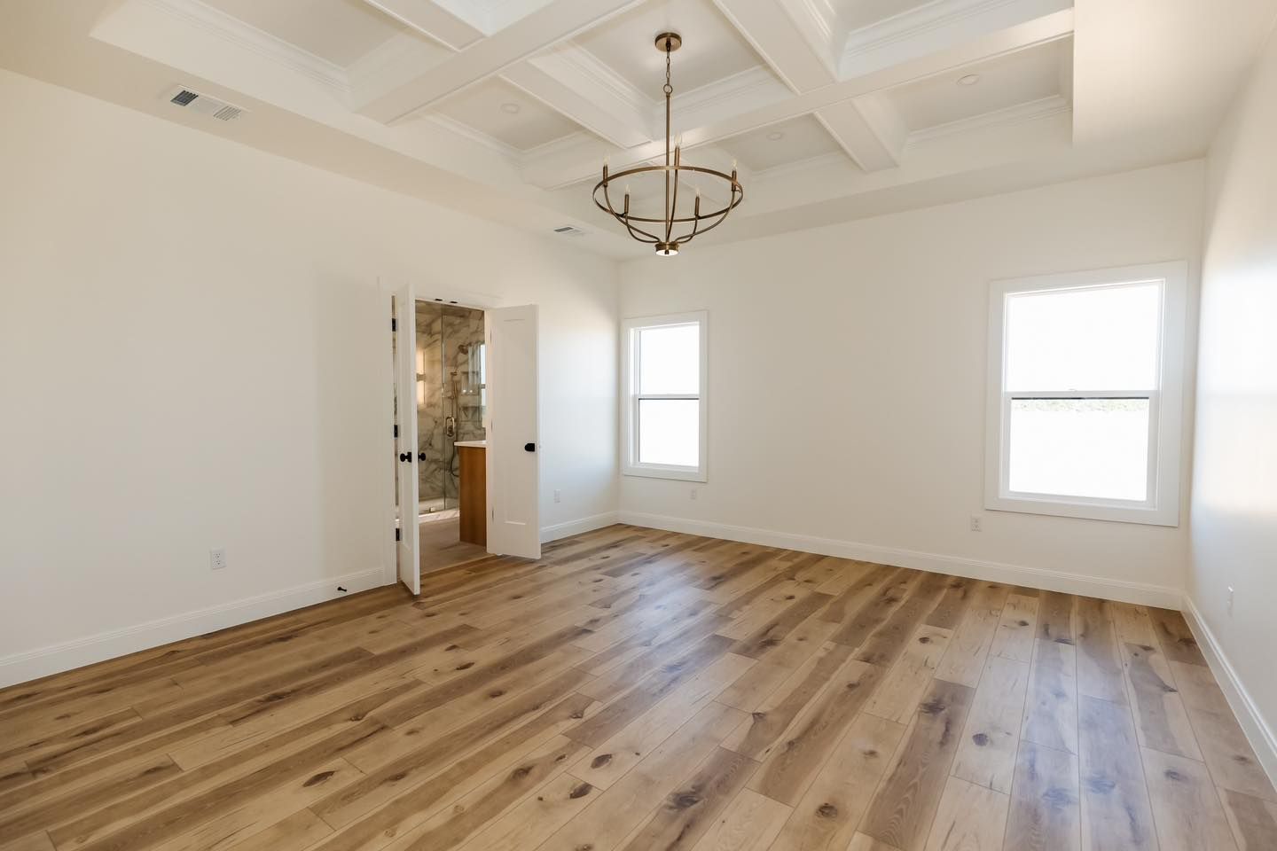 A large empty room with hardwood floors and a chandelier.