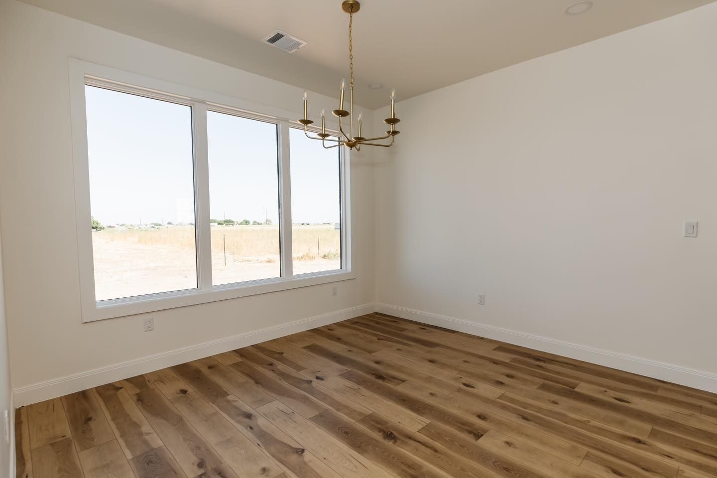 An empty room with hardwood floors and a chandelier.