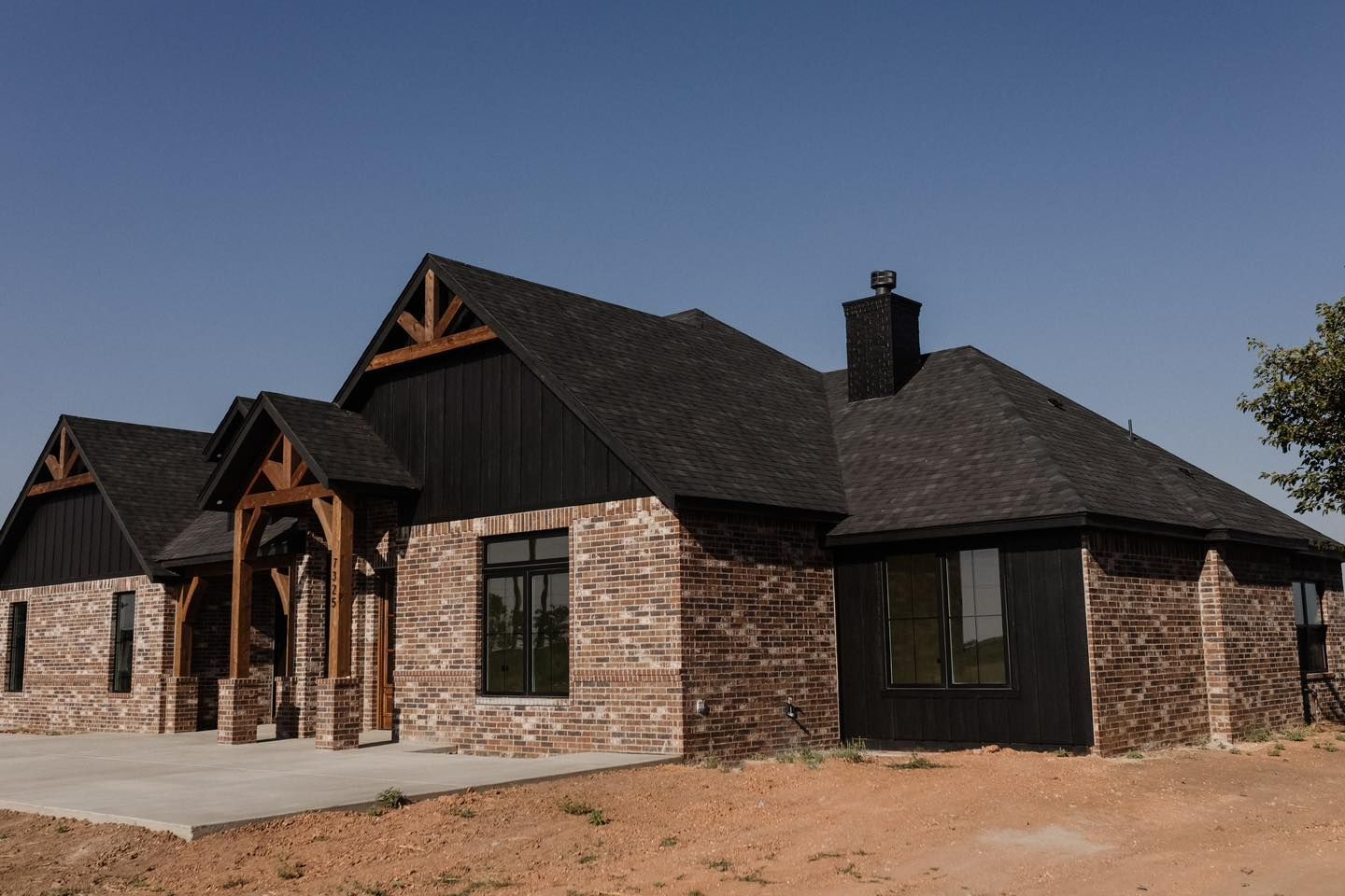 A large brick house with a black roof is sitting on top of a dirt field.
