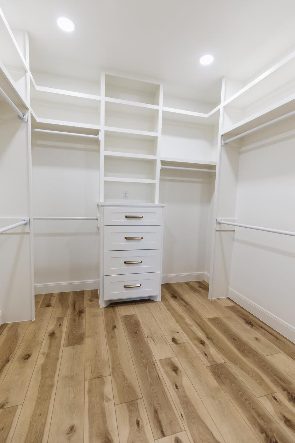 A walk in closet with hardwood floors and white shelves.