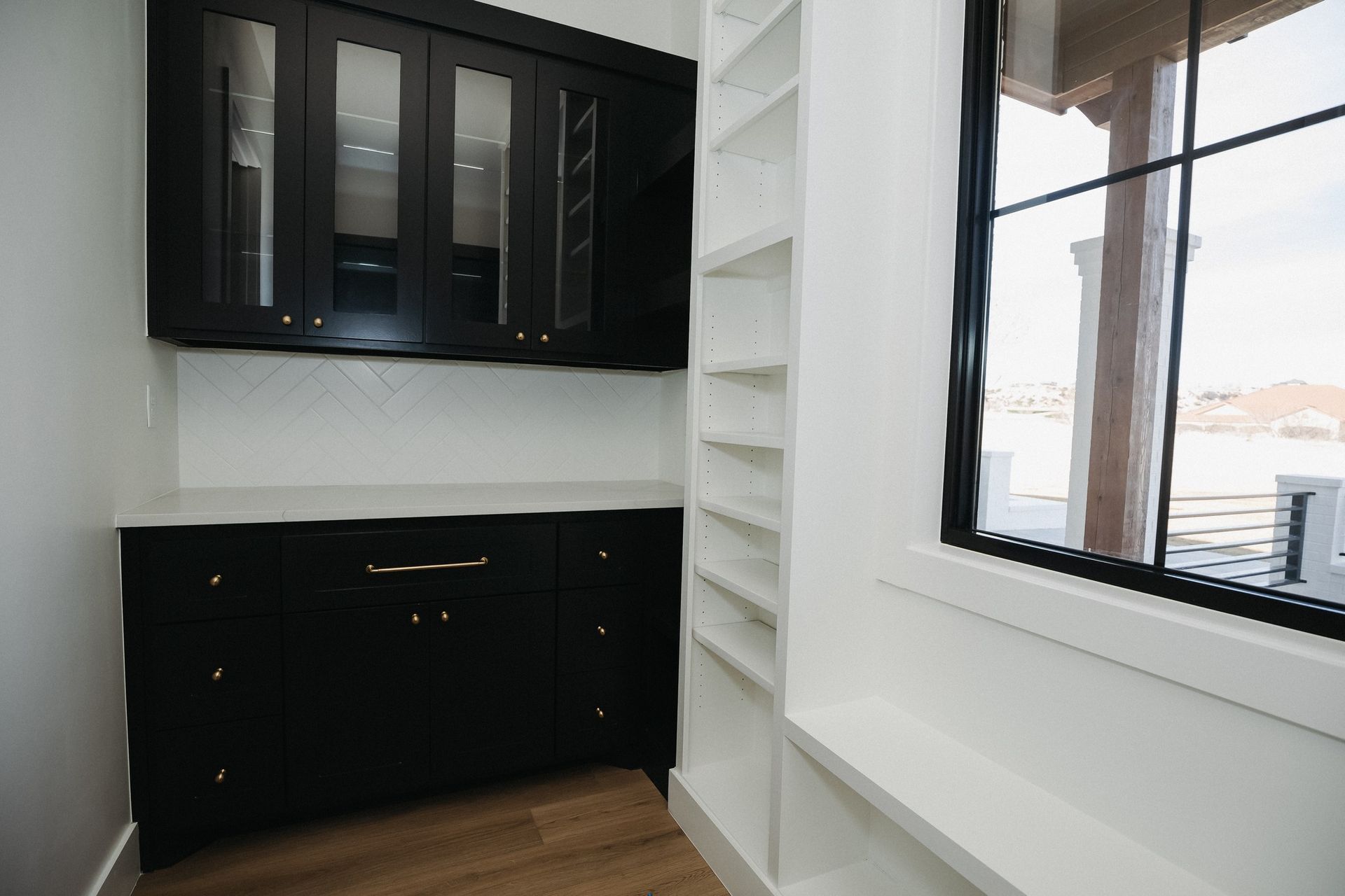 A kitchen with black cabinets and white shelves and a window