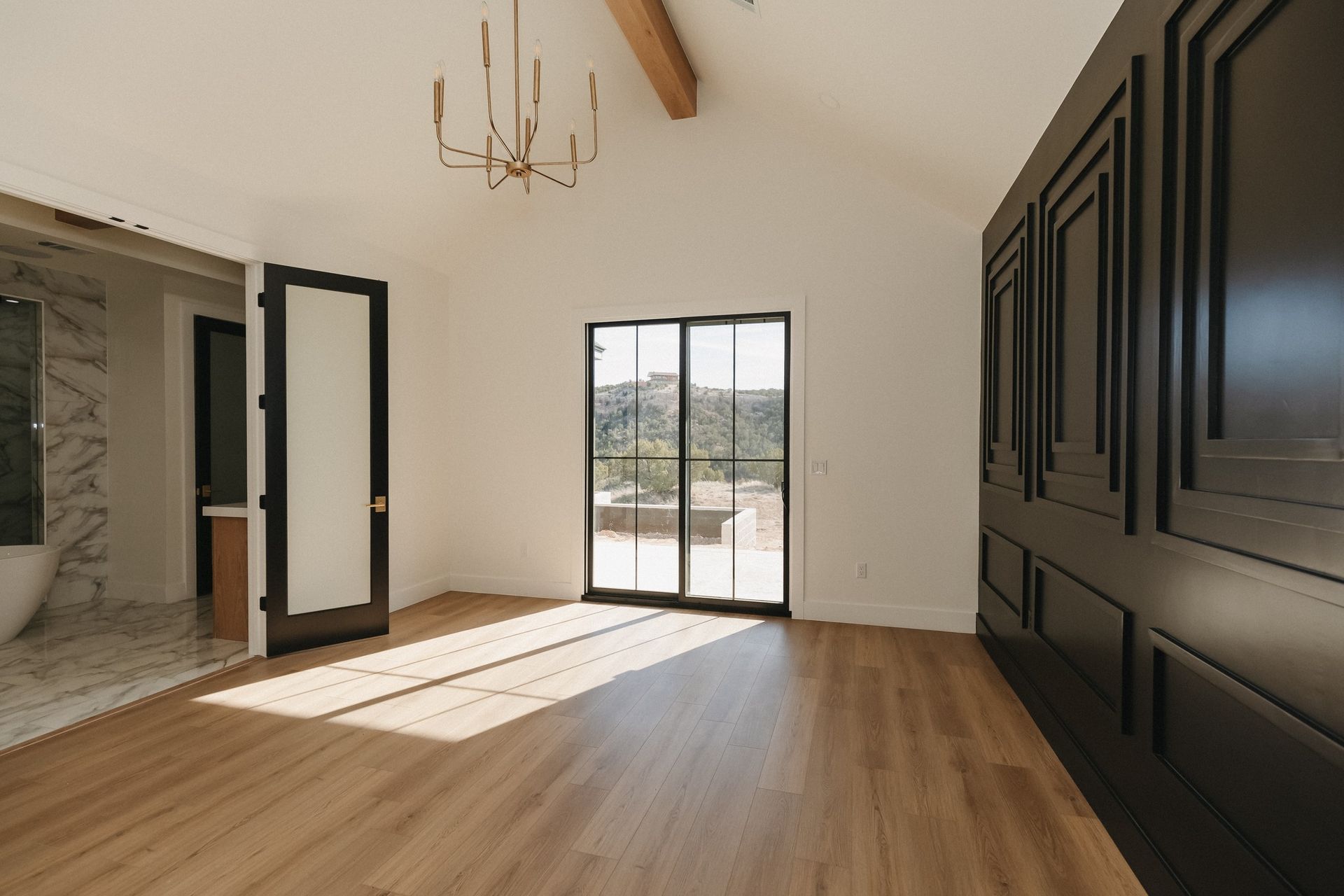 A large empty room with hardwood floors and a chandelier hanging from the ceiling.