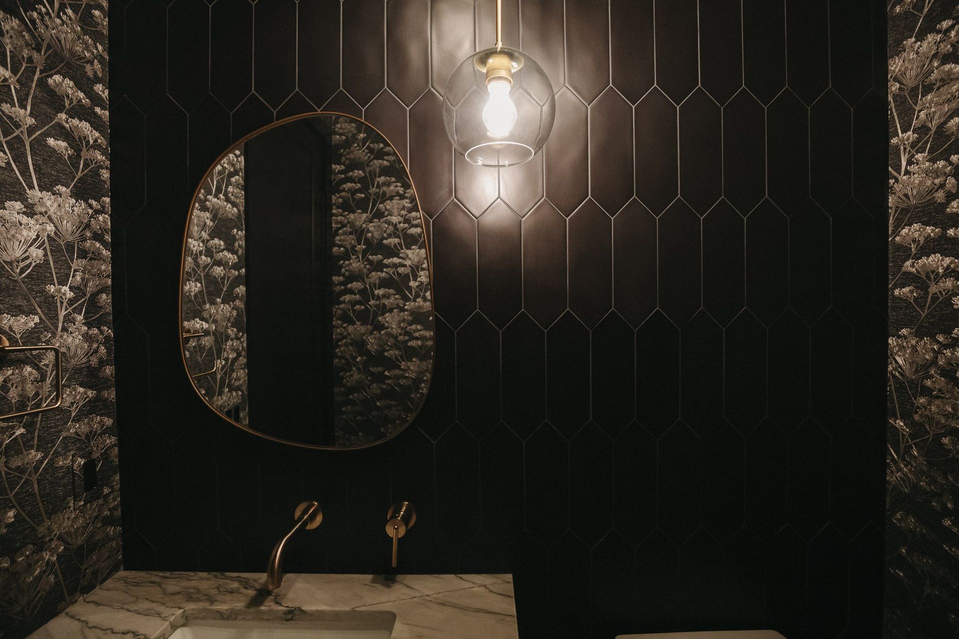 A bathroom with black tiles , a sink and a mirror.