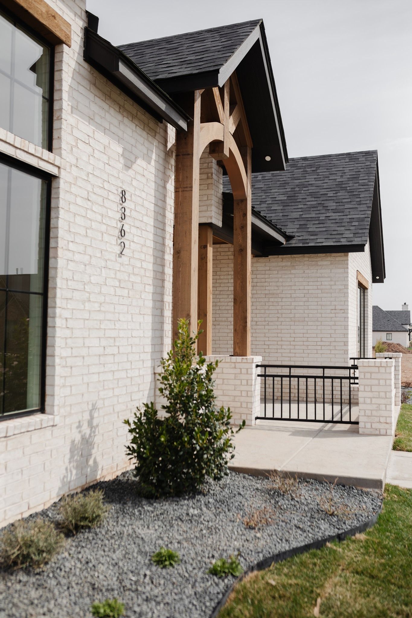 A white brick house with a black roof and a porch.