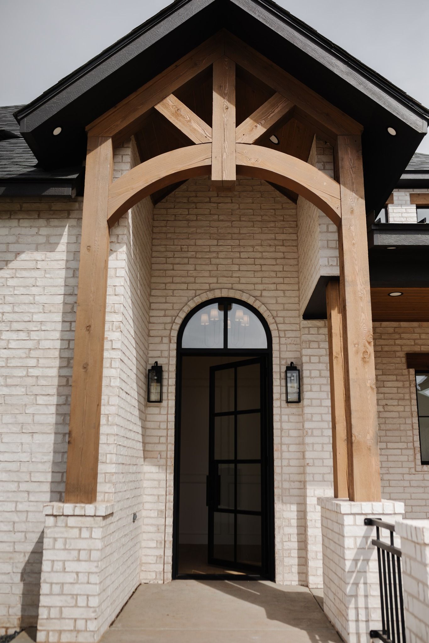 A white brick house with a black door and a wooden archway.