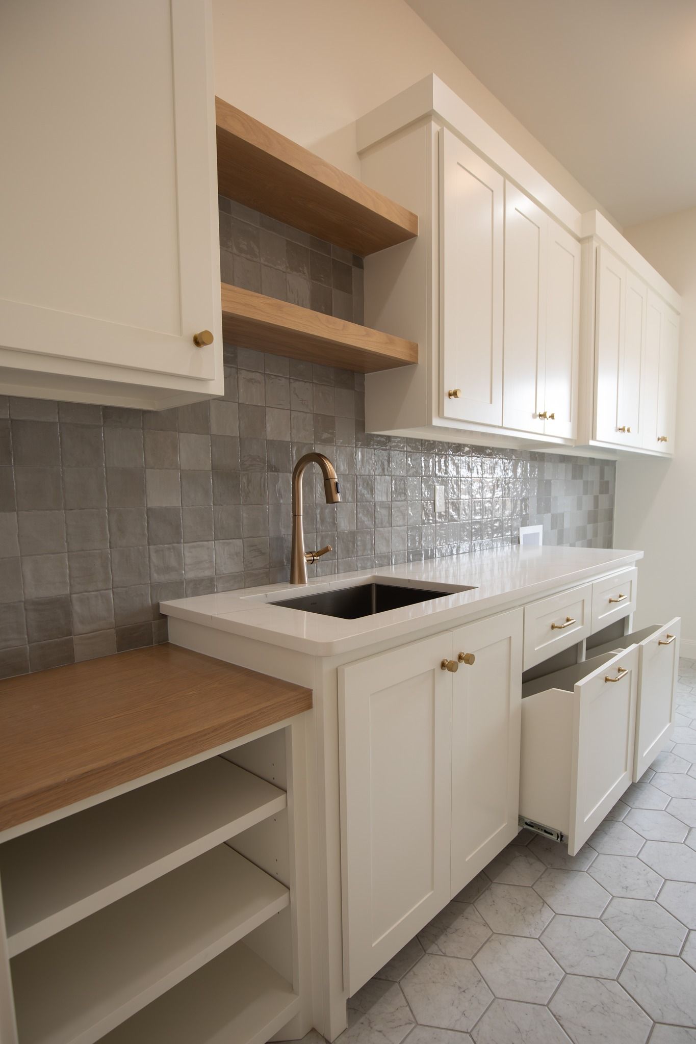 A kitchen with white cabinets , a sink , and wooden shelves.