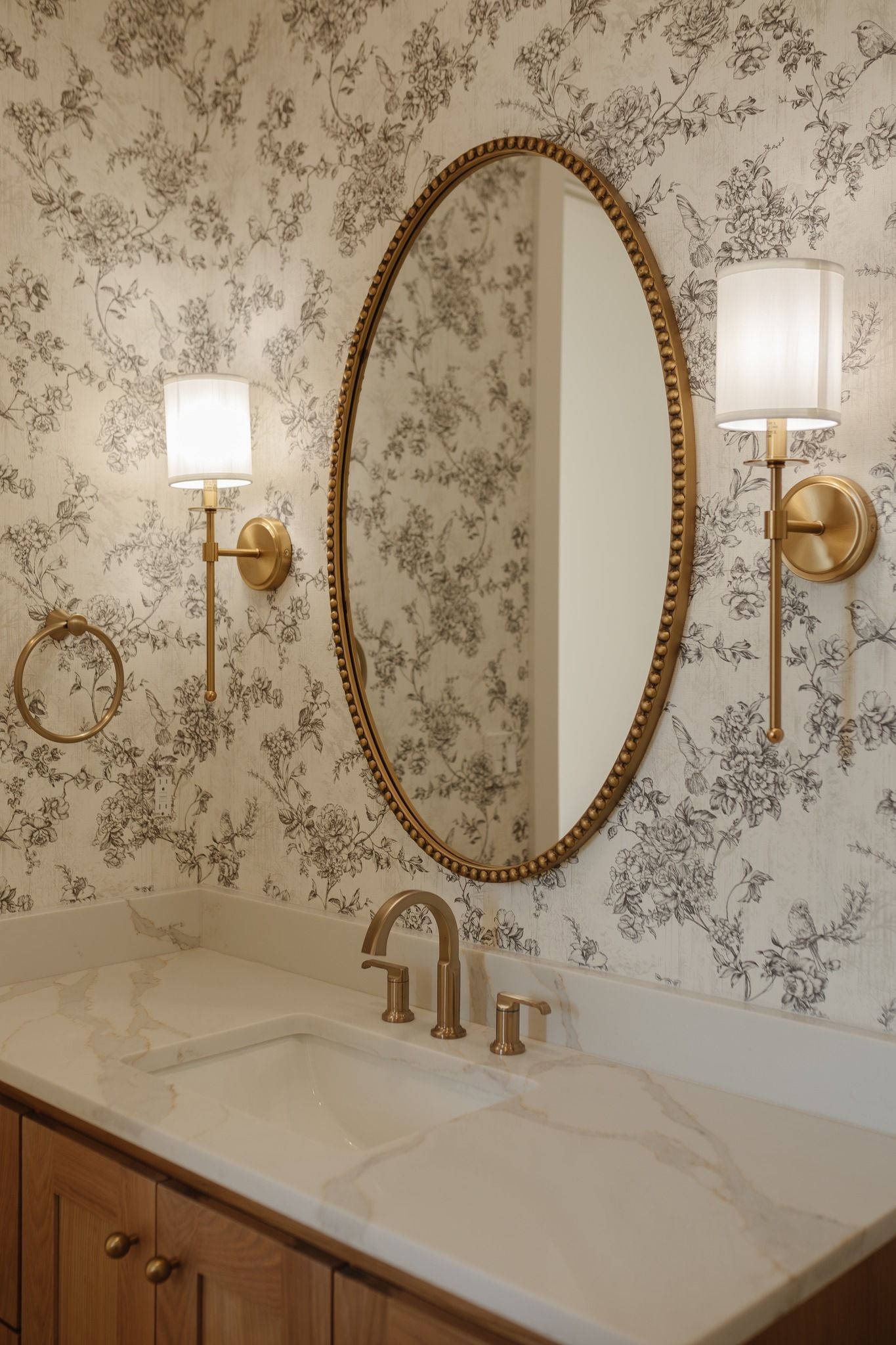 A bathroom with a sink , mirror , and floral wallpaper.