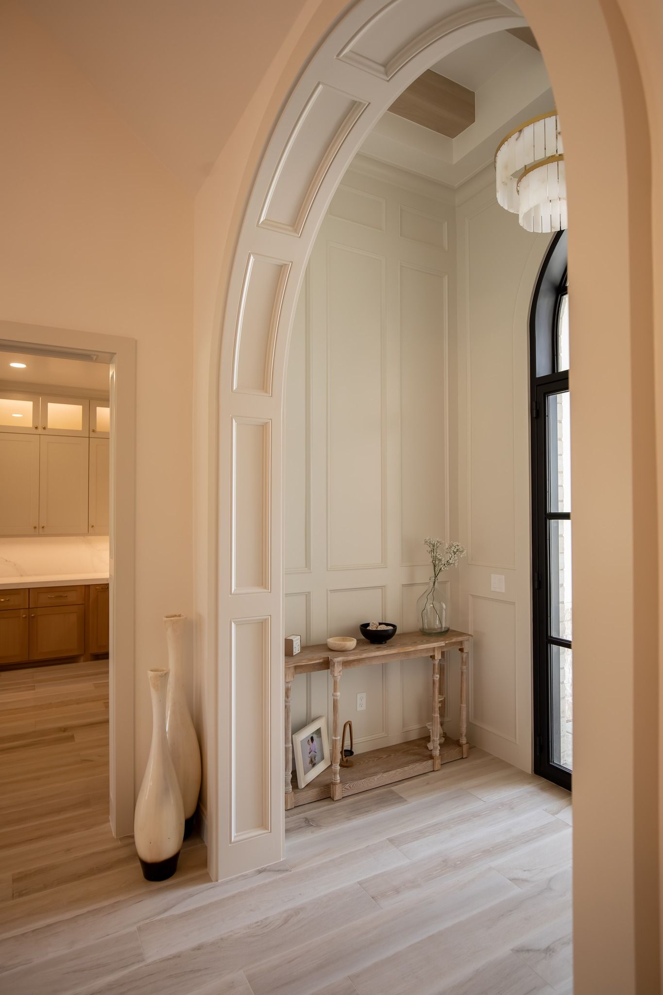 A hallway with a table and vases in it and a window.