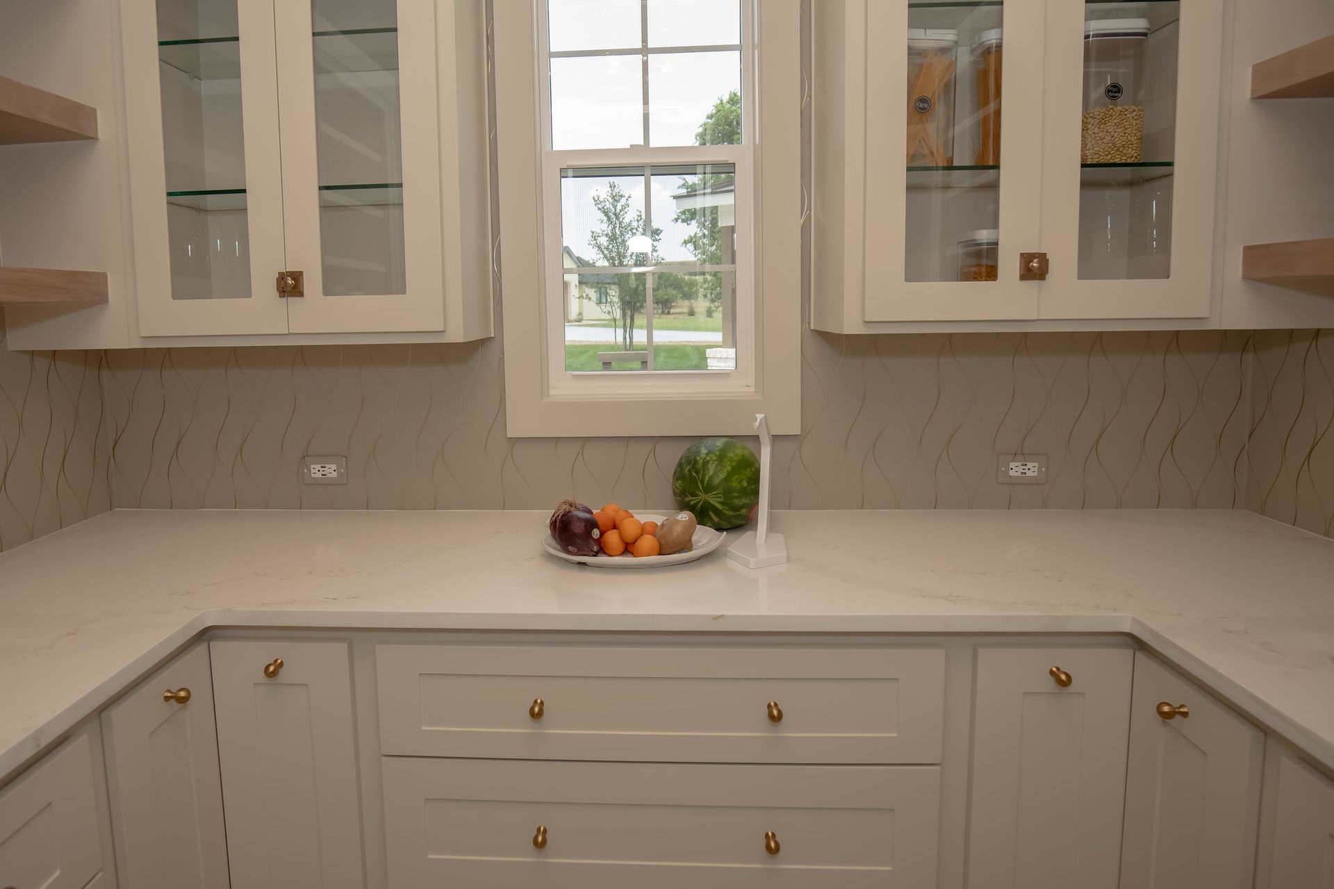 A kitchen with white cabinets and a window with a bowl of fruit on the counter.