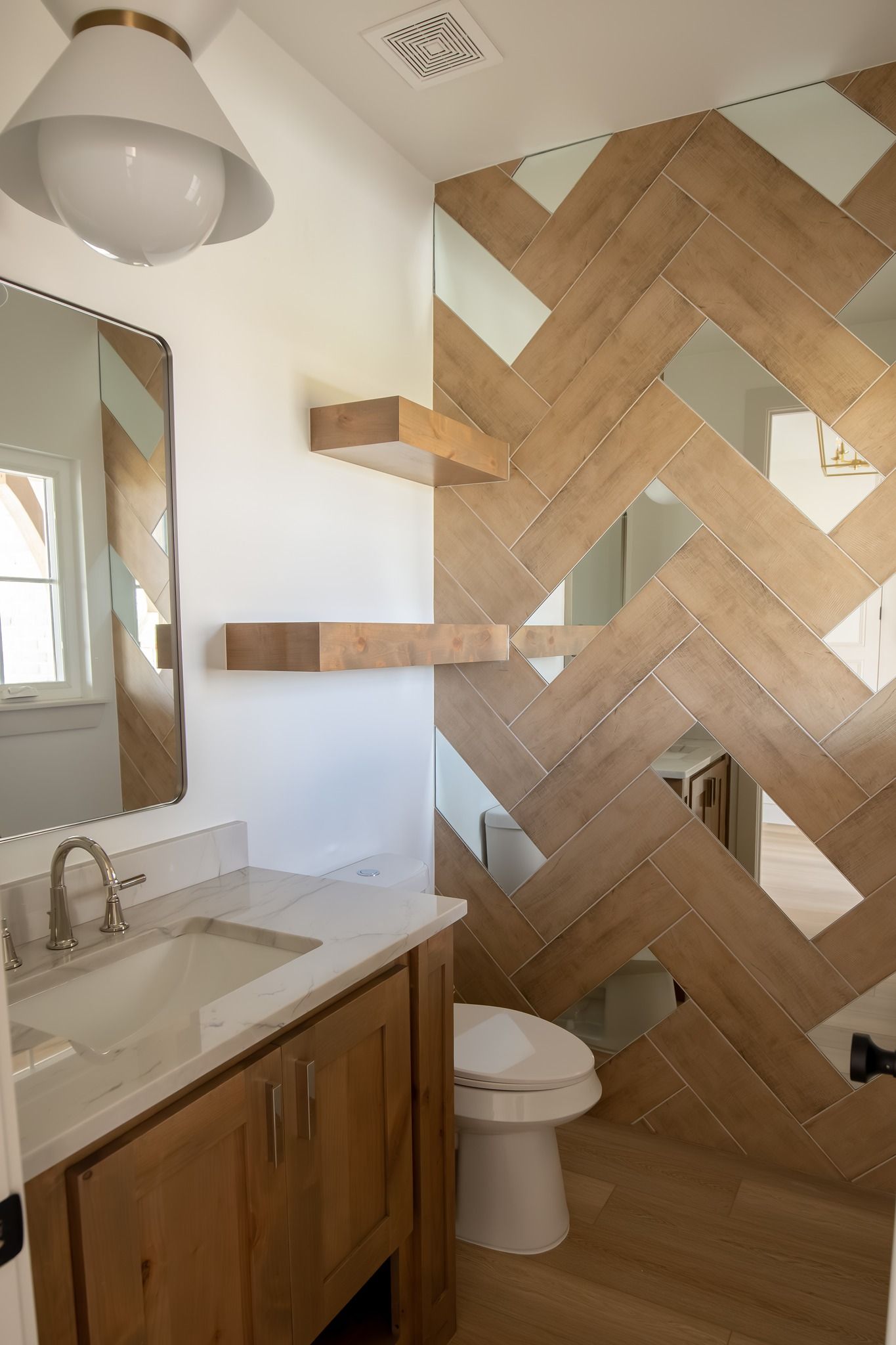 A bathroom with a toilet , sink , mirror and wooden wall.