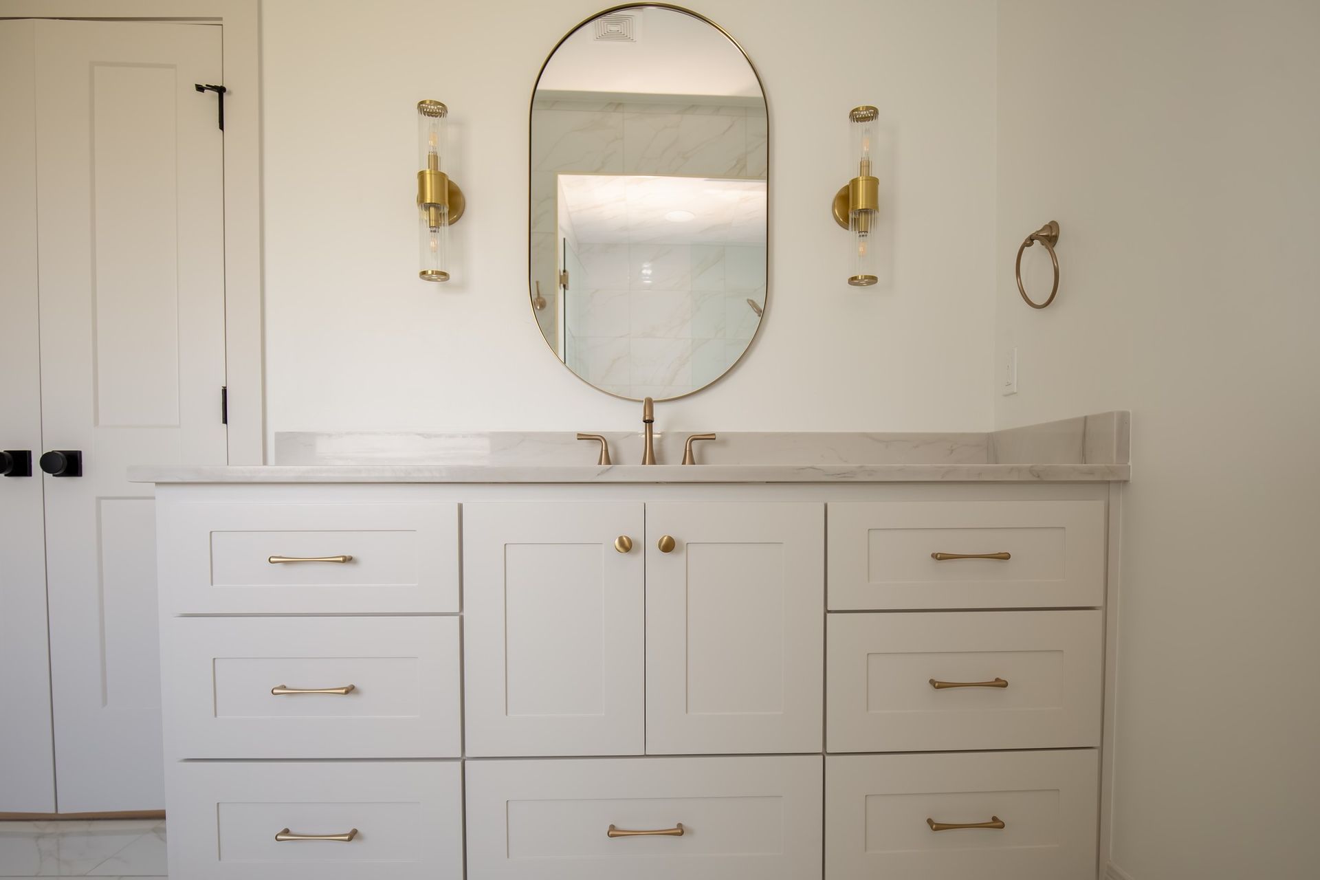 A bathroom with white cabinets , drawers , a sink and a mirror.