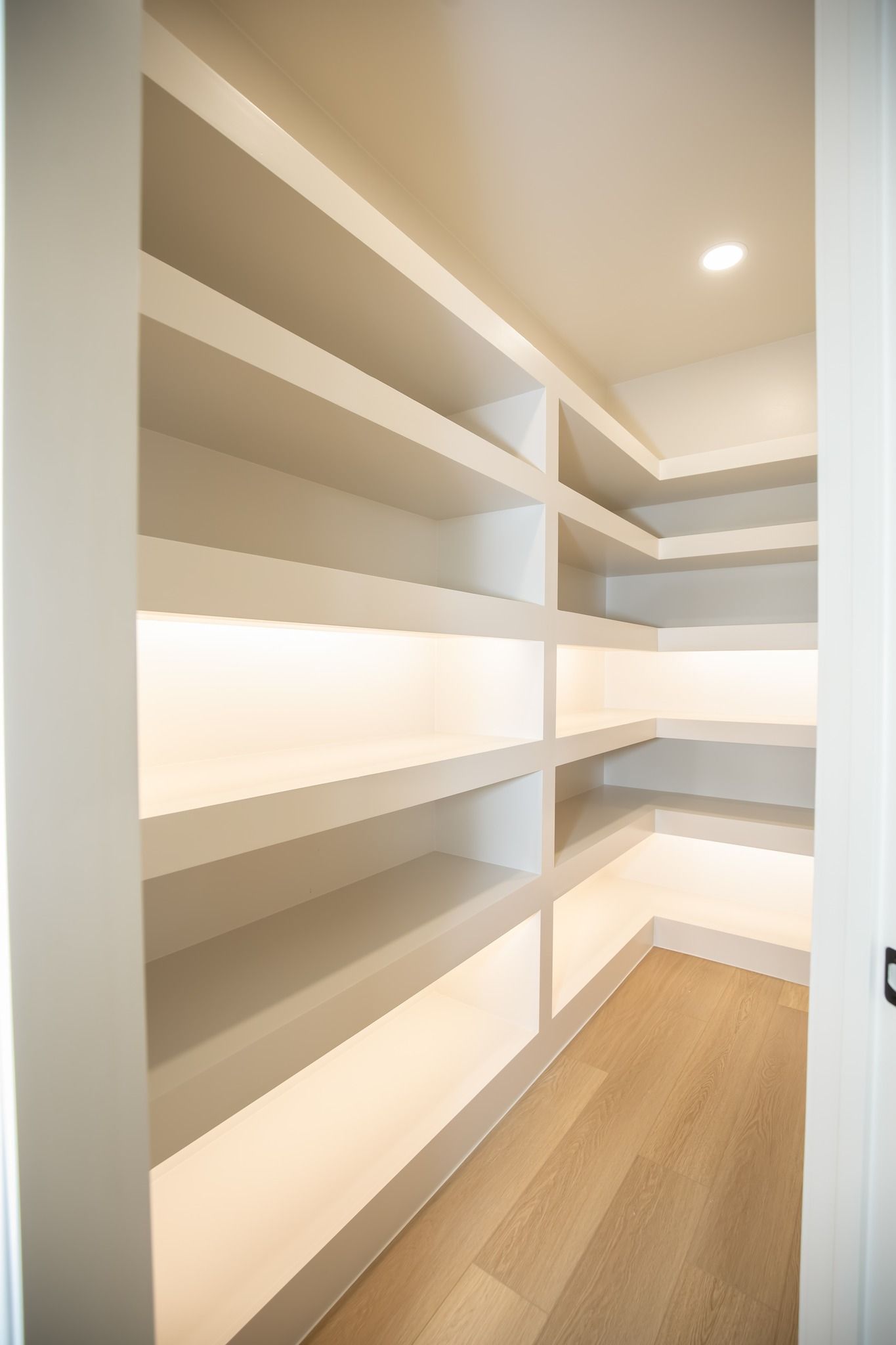 A walk in pantry with lots of shelves and a wooden floor.