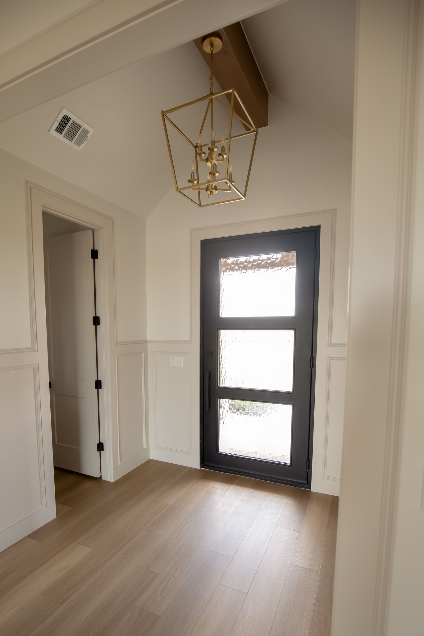 A hallway with a black door and a lantern hanging from the ceiling.
