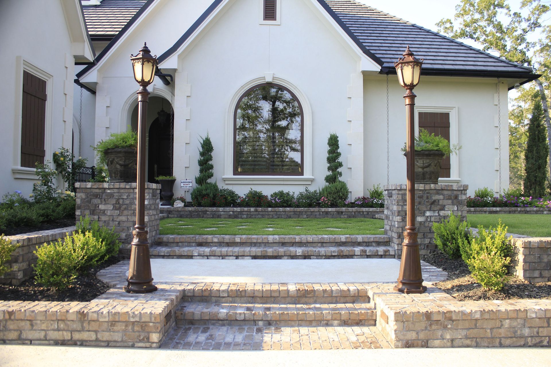 A white house with a brick walkway and two lamp posts in front of it