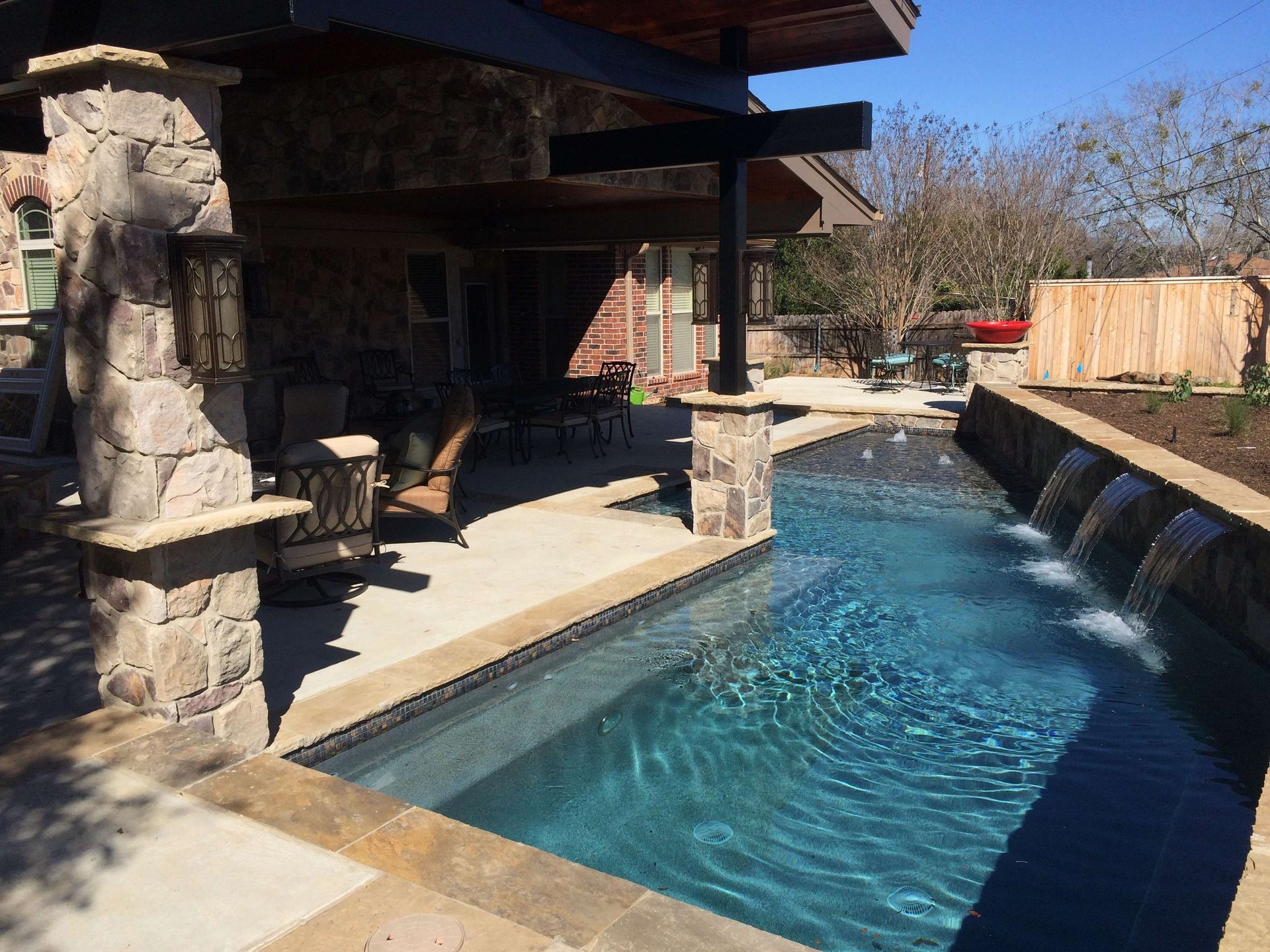 A large swimming pool with a waterfall in the backyard of a house.