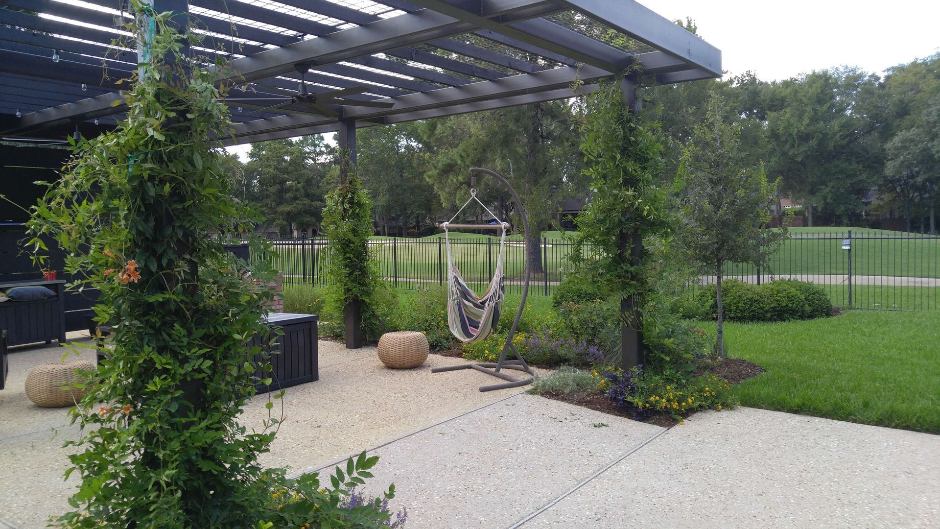 A hammock is hanging under a pergola in a backyard.