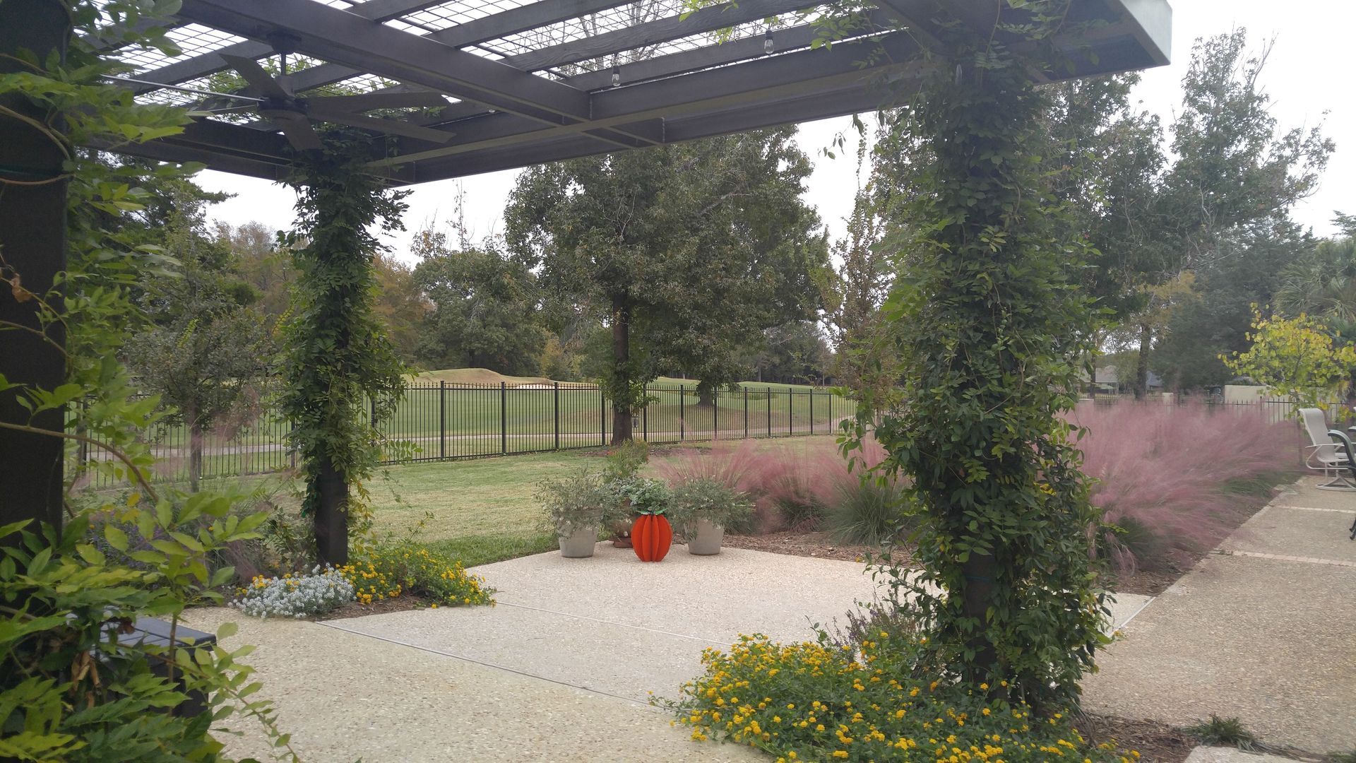 A pergola is surrounded by trees and flowers in a garden.