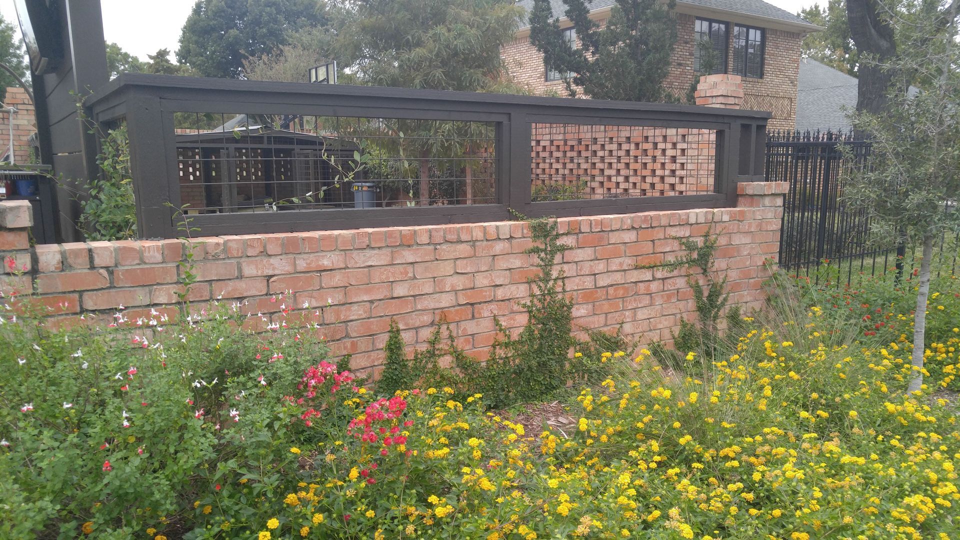 A brick wall with a fence and flowers in front of it