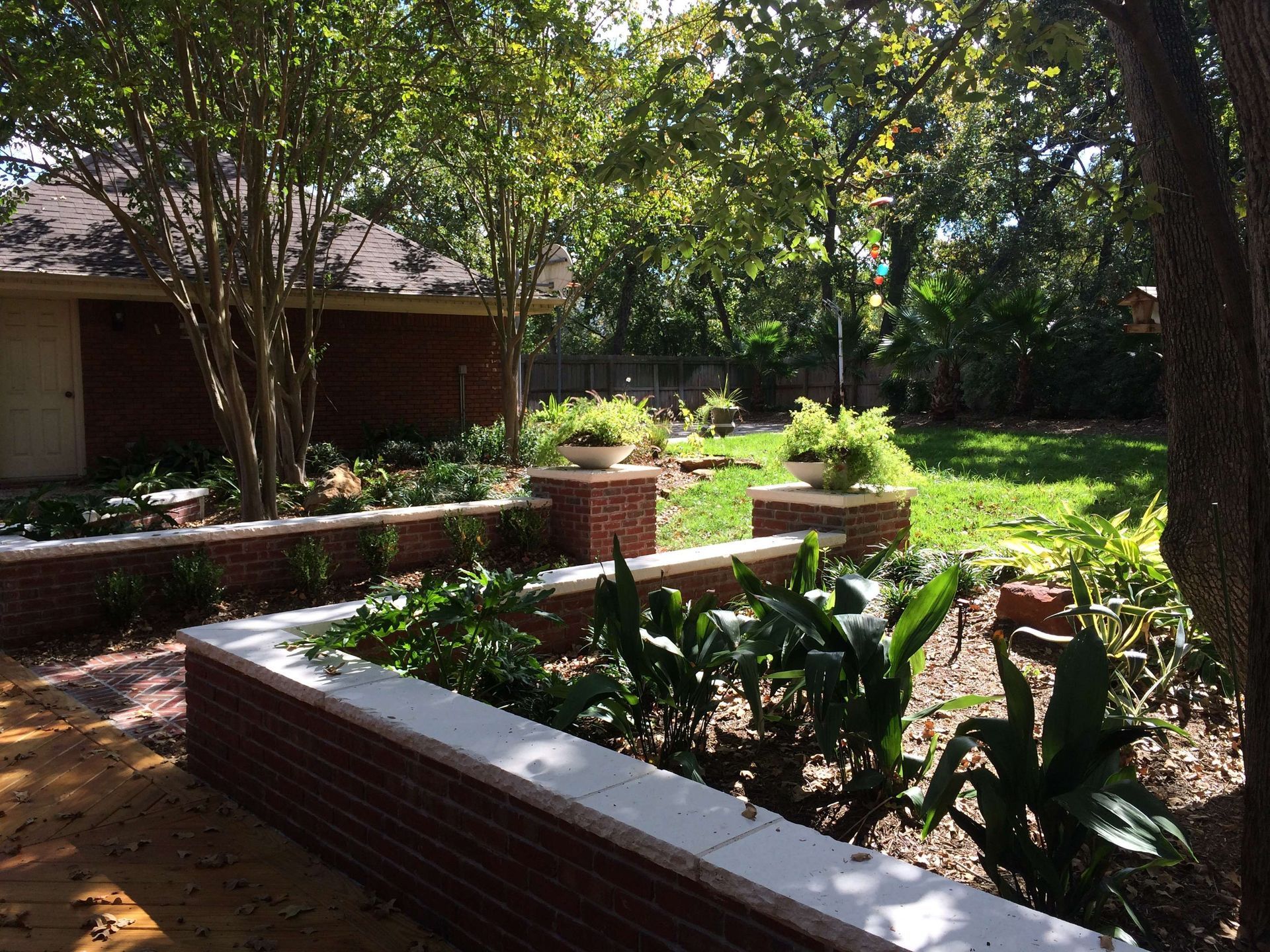 A backyard with a brick wall surrounded by plants and trees