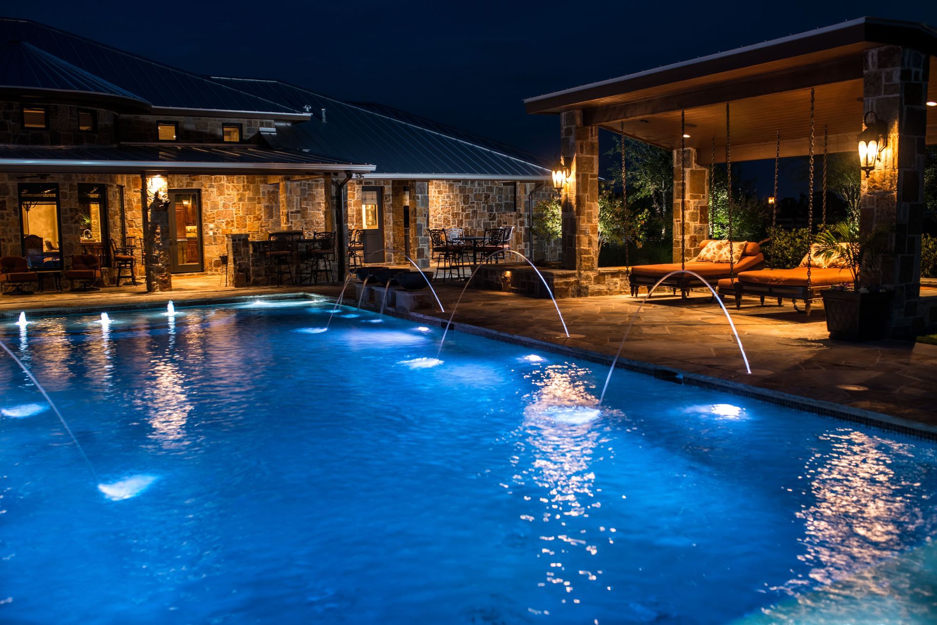 A large swimming pool is lit up at night in front of a house.