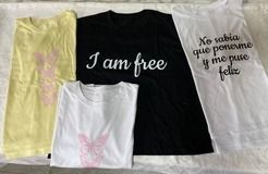 Cuatro camisetas dobladas: una camiseta amarilla y blanca con diseños rosas, una camiseta negra con
