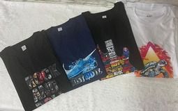 Cuatro camisetas dobladas: negra, azul marino, negra y blanca. Cada una tiene un diseño gráfico en la parte delantera.