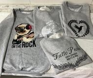 Cuatro sudaderas grises con diseños gráficos: un pug, un colibrí y texto.