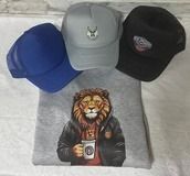 Tres gorras en azul, gris y negro, encima de una sudadera gris con un gráfico de un león sosteniendo una taza de café.