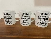 Tres tazas blancas sobre una superficie de madera, cada una con una cita negra en español sobre obstáculos y límites.