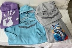 Cuatro sudaderas con capucha en varios colores: huella de mano morada, azul claro con texto, gris con texto y gris con diseño de lobo.
