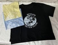 Tres camisetas: amarilla, azul y negra. La camiseta negra tiene un gráfico de luna y el texto