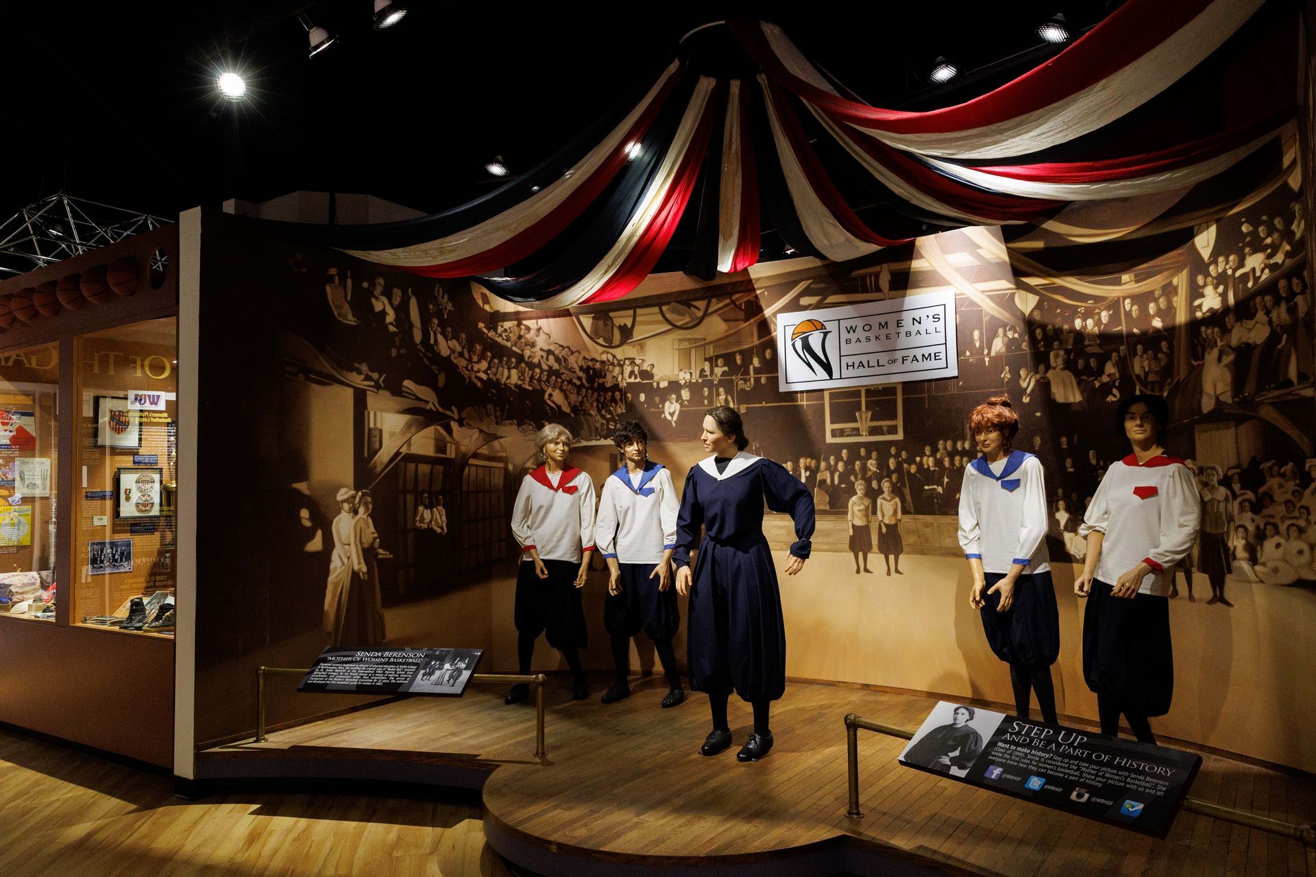 Museum exhibit with mannequins in period clothing under red-and-white draped ceiling lights