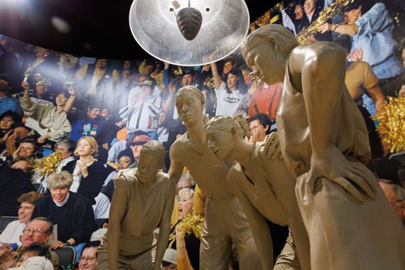 Bronze statues of people beneath a mirrored disco ball, with a colorful crowd mural in the background