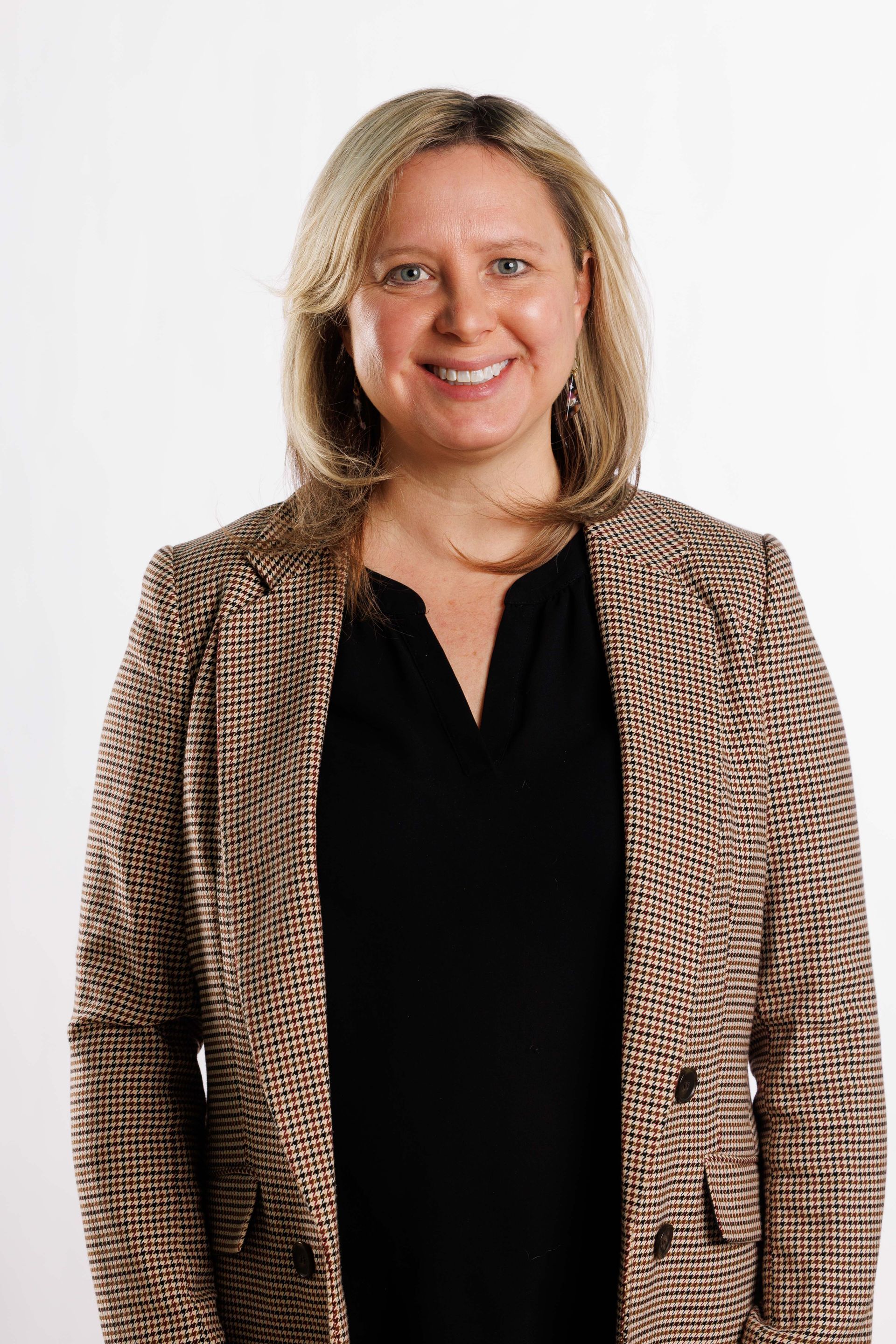 Woman smiling in a black top and patterned blazer against a white background