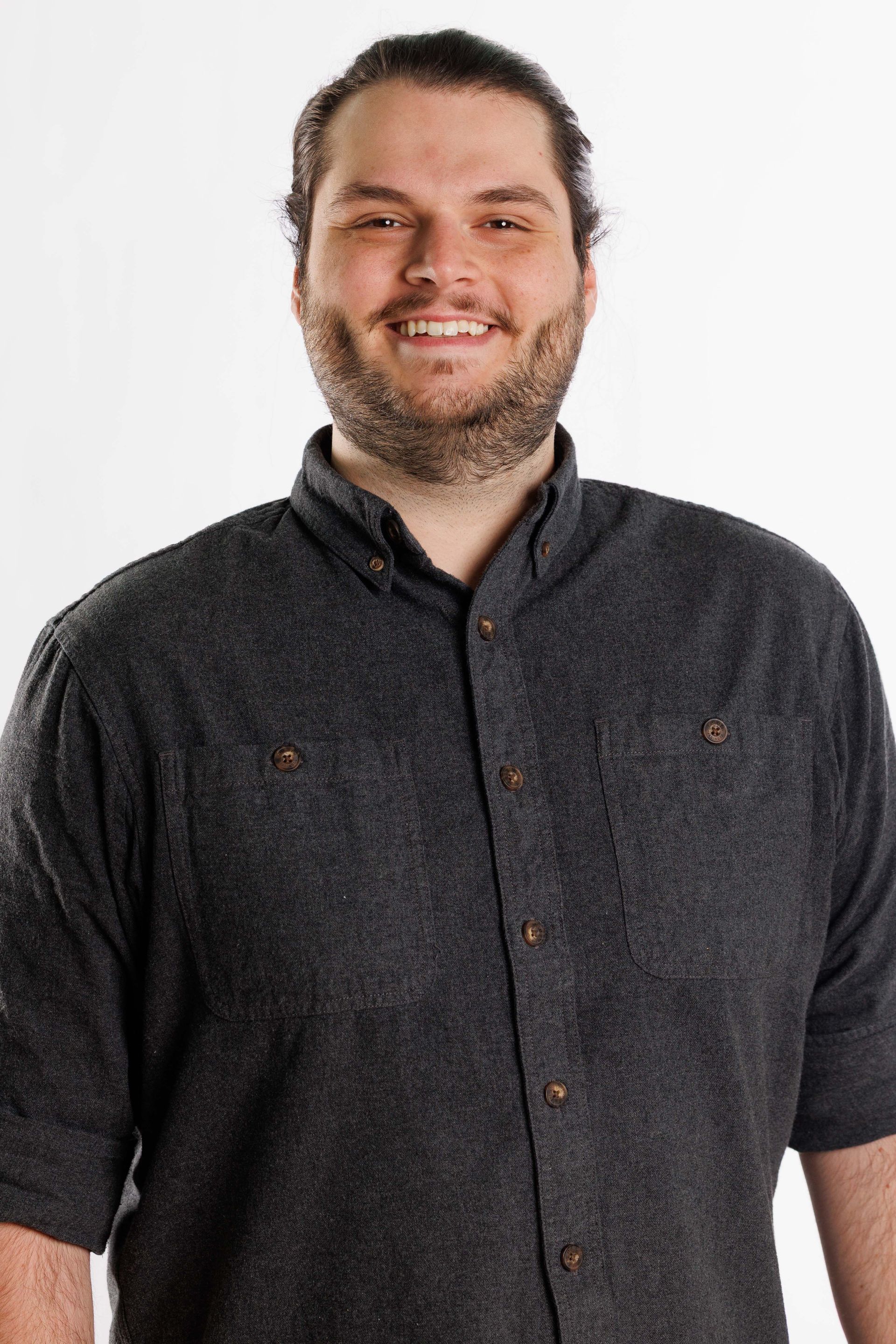 Smiling man in a dark button-up shirt standing against a white background