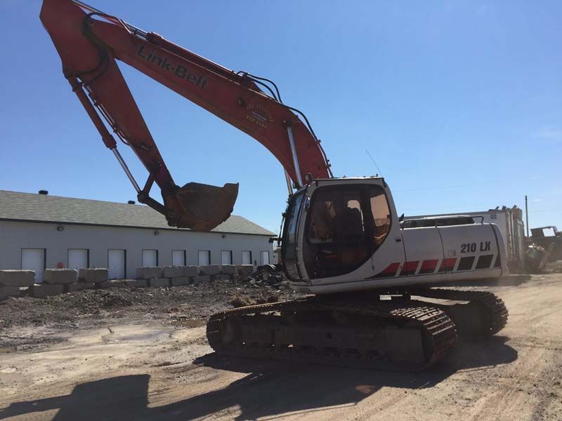 Une grande excavatrice est garée dans un terrain sale devant un bâtiment