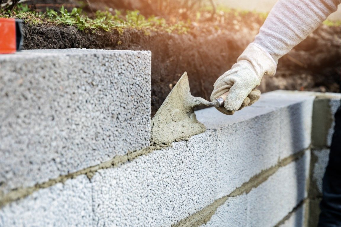 Person wearing gloves laying concrete block with a trowel.