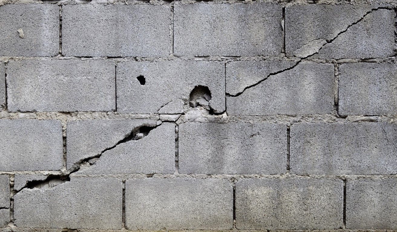 Gray cinder block wall with a large diagonal crack and hole.